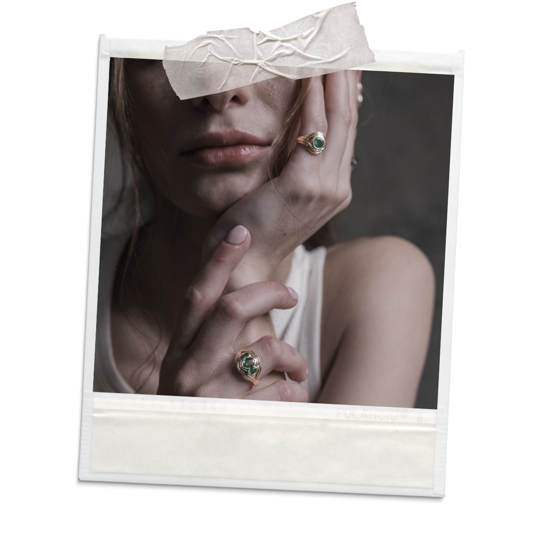 A polaroid picture of a blonde woman that's tightly cropped to reveal only the bottom half of her face and two hands, both of which are sporting gold and gemstone rings. 