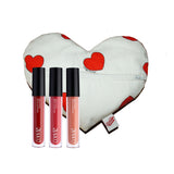 A white heart-shaped makeup bag with red heart print, with 3 lipglosses standing up alongside it